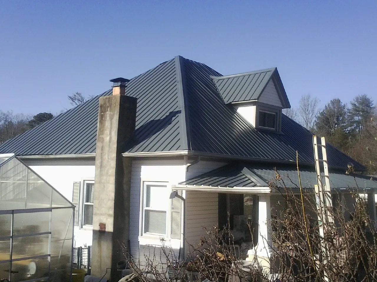 Dark blue standing seam metal roof on a white farmhouse with dormer — Slate & Tile Roof Repair by Roofing Brothers in Lakewood