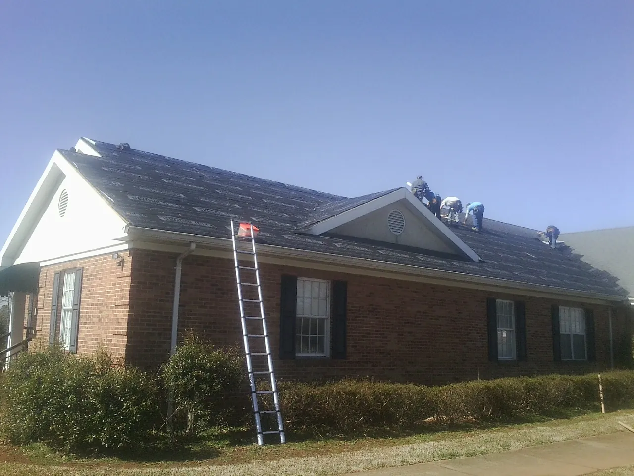 Crew tearing shingles off a brick ranch roof with a ladder set — Emergency Roof Repair work by our crew in Lakewood