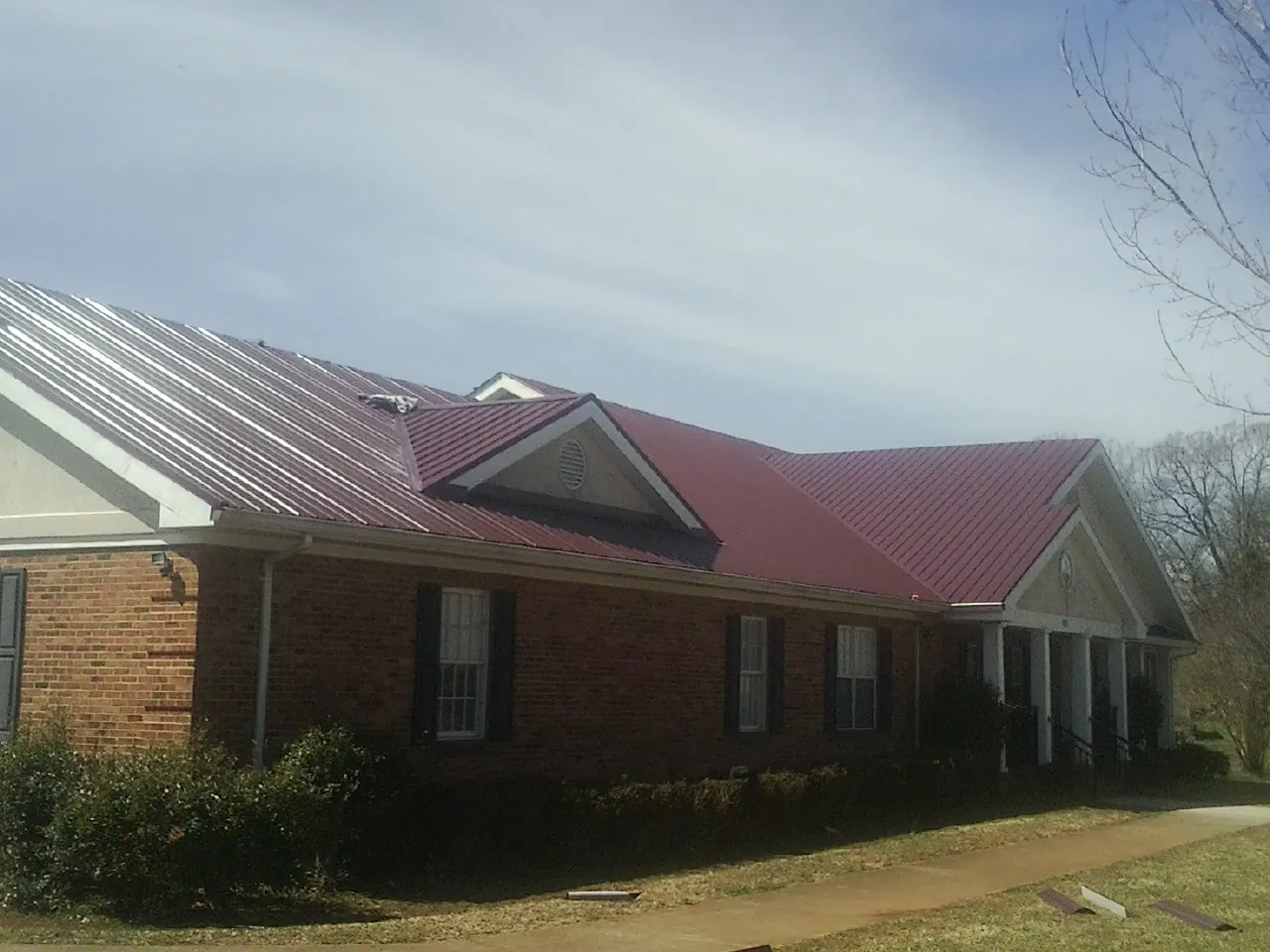 Red metal roof with gabled entries on a long brick building, from a Hail Damage Roof Repair job in Lakewood