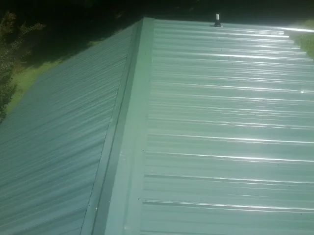 New green metal panels meeting at the ridge of a roof — Flat Roof Repair work by our crew in Lakewood